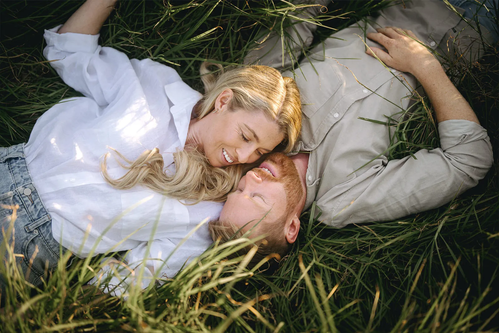 Playful engaged couple lying together in long grass