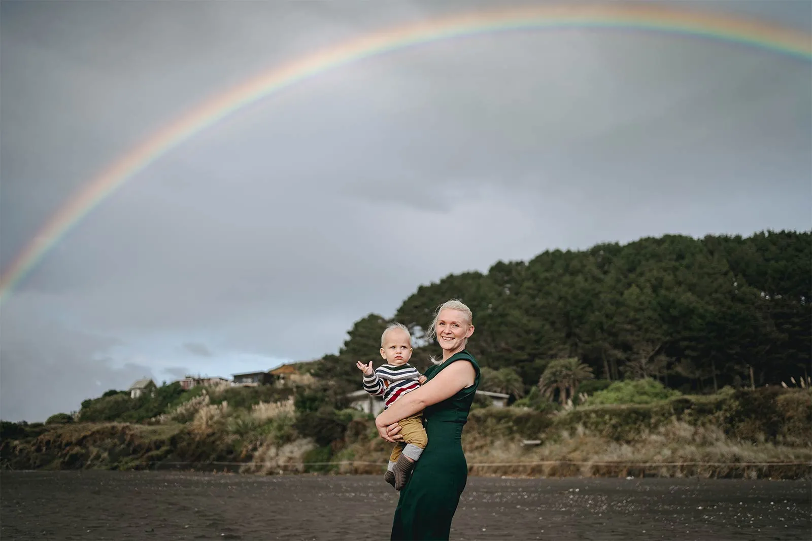 Mother and baby beneath a rainbow at the beach