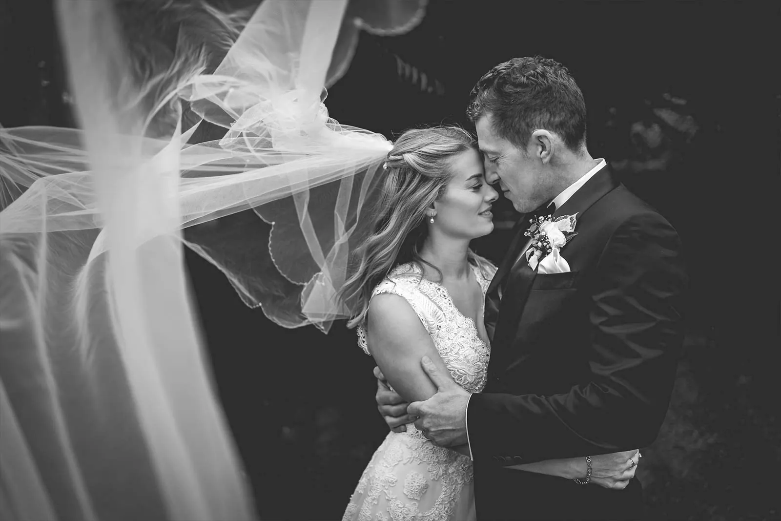 Black and white wedding portrait beneath a flowing veil