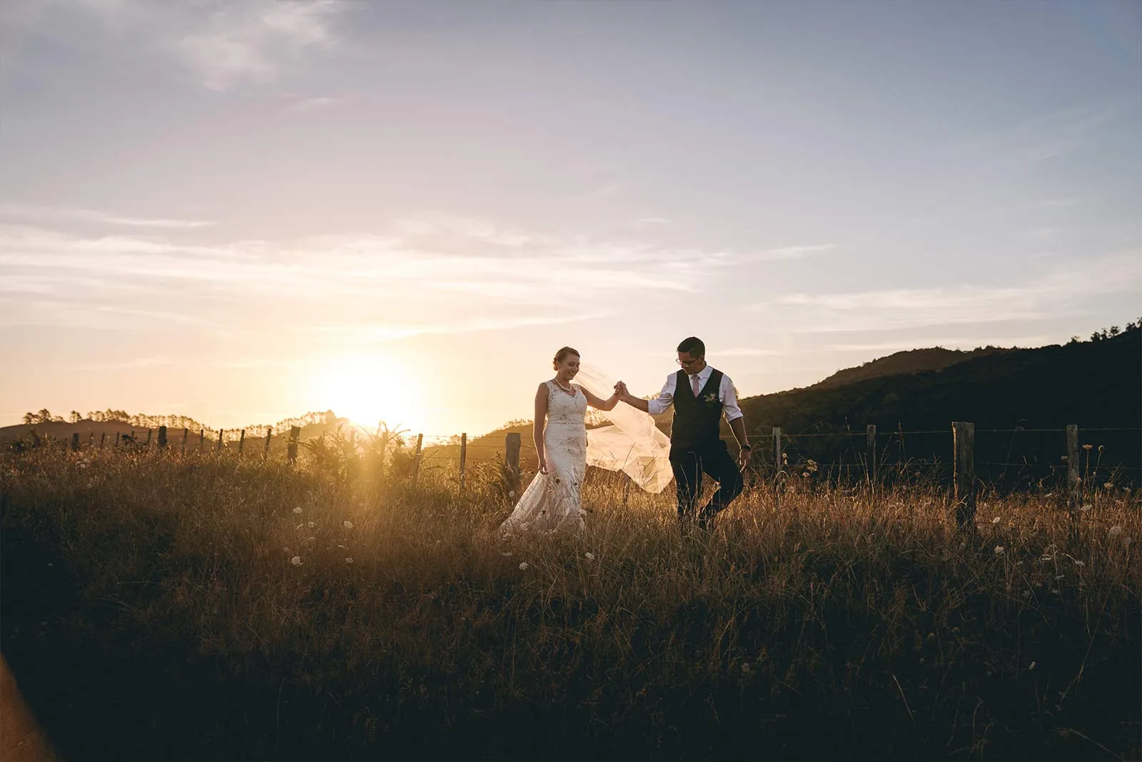 Wedding couple walking through a field at sunset